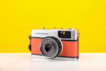 Load image into Gallery viewer, Olympus Trip 35 vintage 35mm film camera with orange leather skin and a Zuiko 40mm f2.8 lens, displayed against a yellow background.