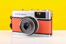 Load image into Gallery viewer, Olympus Trip 35 vintage 35mm film camera with orange leather skin and a Zuiko 40mm f2.8 lens, displayed against a yellow background.