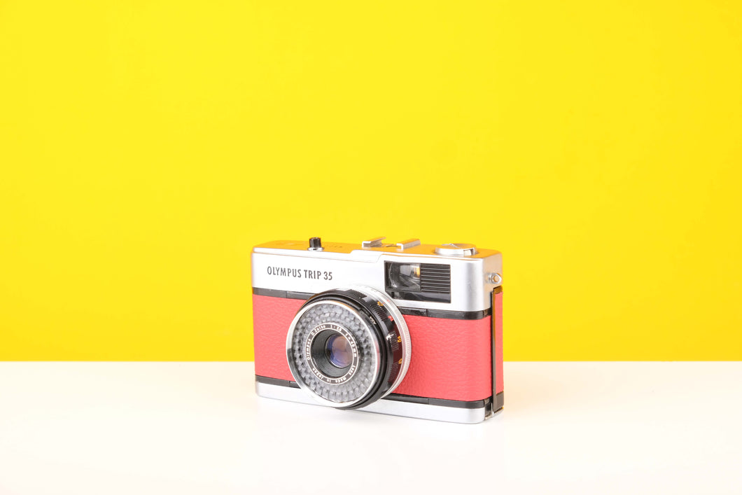 Olympus Trip 35 vintage film camera with customized red skin, displayed against a yellow background.