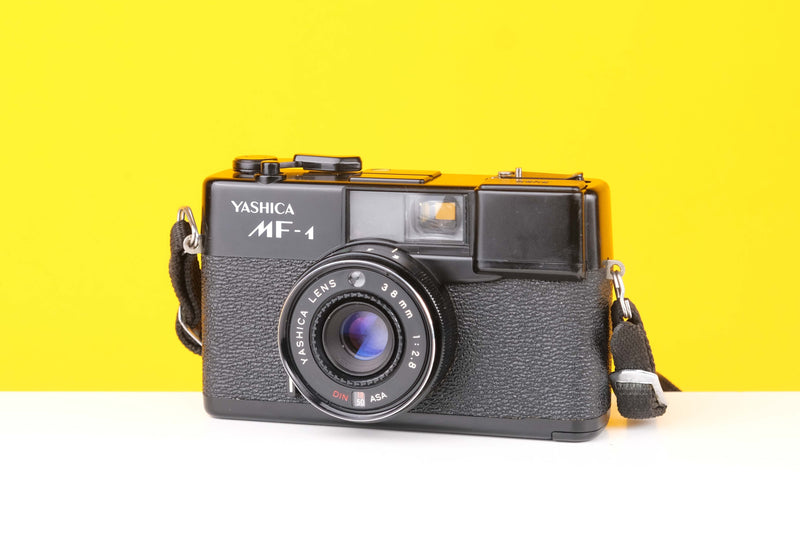 Yashica MF-1 35mm viewfinder film camera with a black body, visible focus zone setting, and a lens.